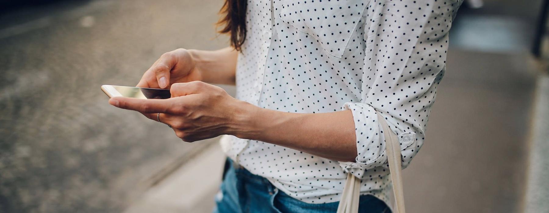 woman walks down the street and texts with a bag of groceries on her arm